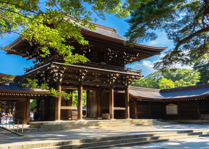 Meiji Jingu Shrine on a sunny day, framed by lush, green trees.